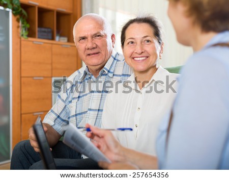 Smiling elderly couple talking with employee with laptop at home. Focus on man