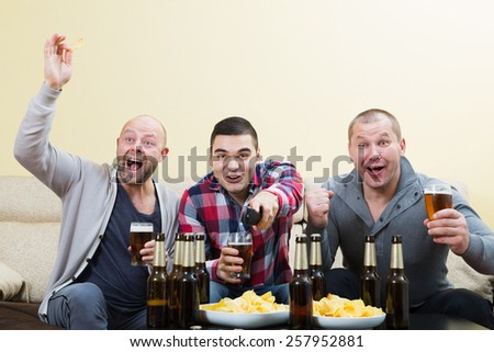 Three adult european male friends sitting at table with beer and commenting sport tv channel