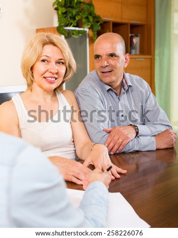 Smiling mature couple listening worker of the company at the table