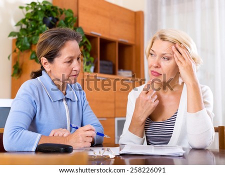 Sad female pensioners discussing finances indoor. Focus on the left woman