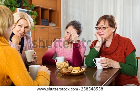 sad senior female friends drinking coffee and sharing problems at table  indoor