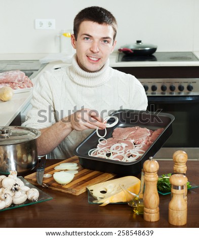 Smiling guy with raw meat at home kitchen