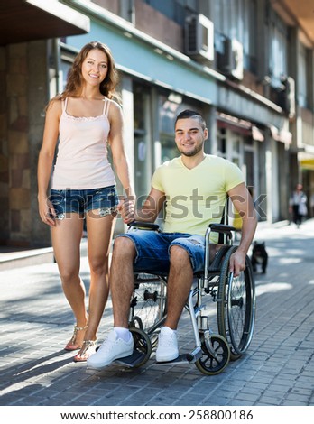 Positive woman and her disabled husband in wheelchair outdoor
