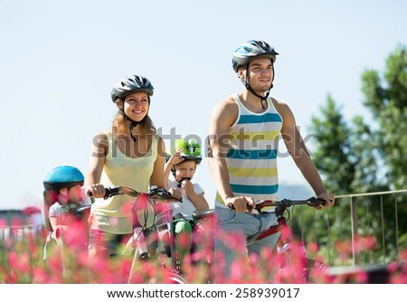 Smiling young family of four cycling on street road in summer day