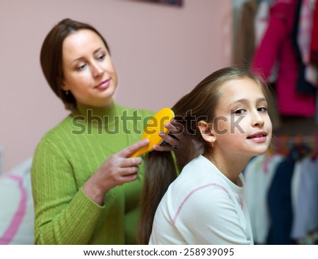 Mom taking care of little daughter hair with brush