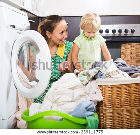 Home laundry. Smiling mother with little child using washing machine at home