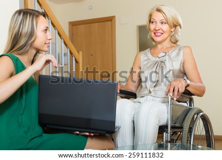 Social worker with laptop questioning handicapped smiling woman. Focus on mature