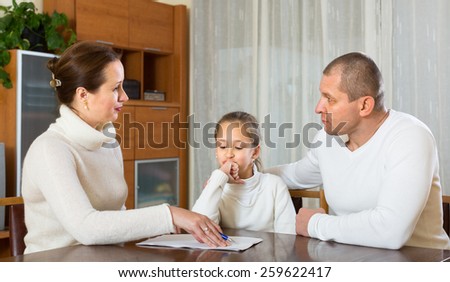 Sad family with little daughter reading financial documents at table