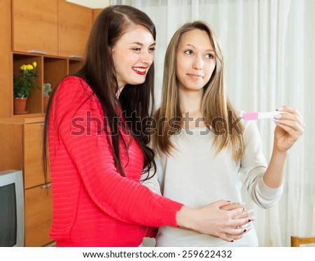 Smiling girls with pregnancy test at home interior. Focus on blonde