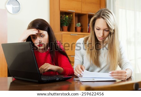 serious women looking  documents with laptop at table in home interior