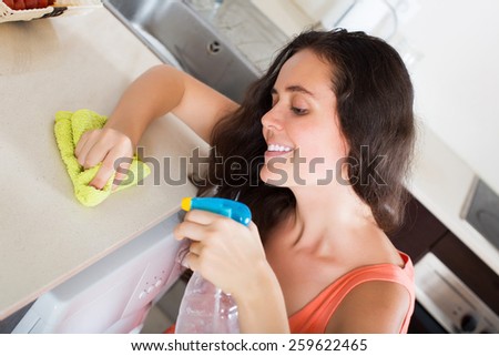Happy young woman cleaning  furniture in kitchen at home