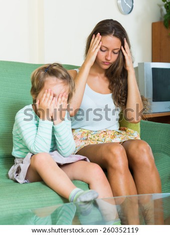 Upset woman and little girl sitting on couch at home. Focus on woman