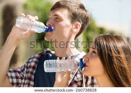 Thirsty young male with girlfriend taking a refreshing drink of water from bottle