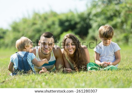 Portrait of happy family of four lying on grass in sunny summer park. Focus on man