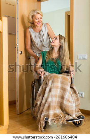 Smiling mother helping handicapped girl to enter the apartment. Focus on young
