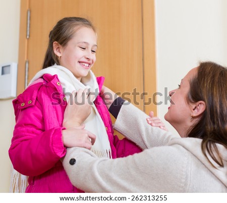 Loving and careful woman dressing daughter warmly before off