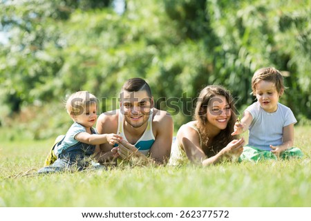 Happy family with two kids lying on grass in sunny summer park. Focus on man