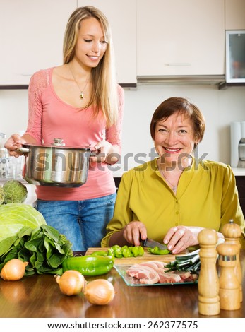 Happy mature woman with adult daughter cooking   at  kitchen. Focus on mother