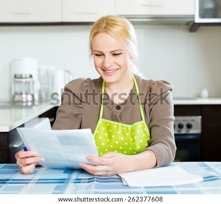 Happy young woman reading documents at kitchen