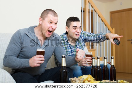 Two excited male sport fans with beer watching hockey game heatedly at home