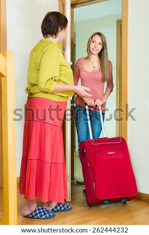 Elderly mother and adult daughter with a suitcase saying goodbye at the door