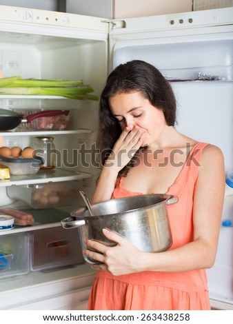 Brunette  female  holding her nose because of bad smell near fridge at home