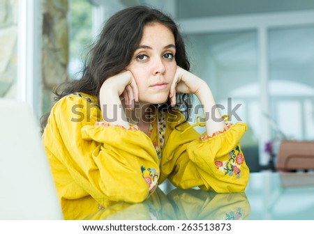 Young long-haired woman in bright blouse sitting sad at home