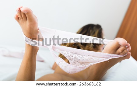 Middle-aged blonde woman takes off underwear on bed