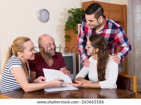 Young happy spouses sitting with documents and asking friends for advice