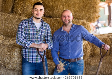 Portrait of two casually clothed farmers with holding pitchforks in a barn near haystack