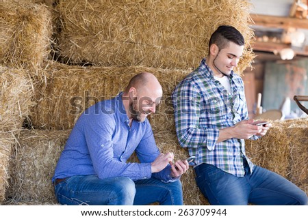 Portrait of two farmers with phones at hayloft. Selective focus
