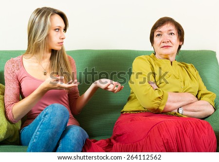 Young daughter and elderly mother sitting on the couch and arguing about something