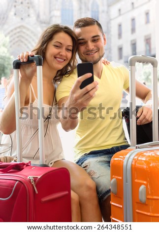 Man and woman with luggage doing selfie during city tour at vacation