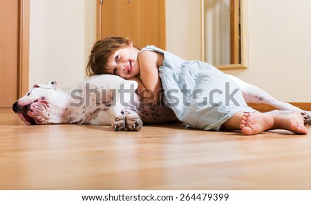Cheerful smiling little girl hugging big white dog at home