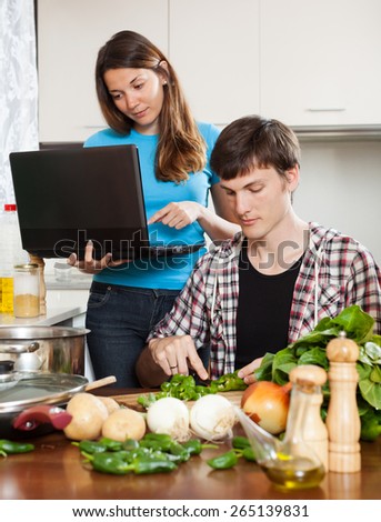 Man cooking food while woman looking at laptop  in home kitchen