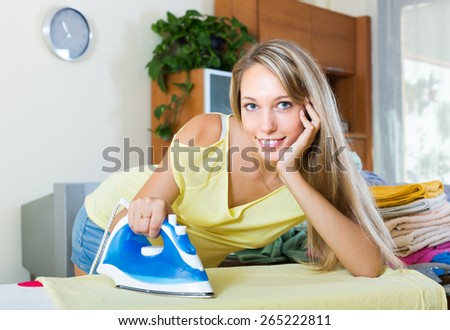 Smiling young housewife ironing at ironing board in home