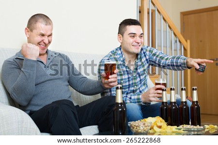 Two excited adult men drinking beer and watching football game indoor