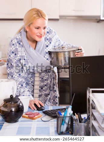 freelancer 30s with dishware working on PC at kitchen