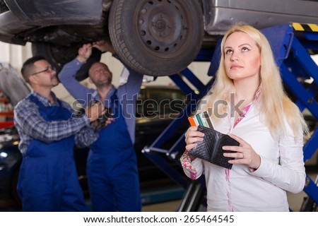 Thoughtful blonde girl with credit cards at auto repair shop