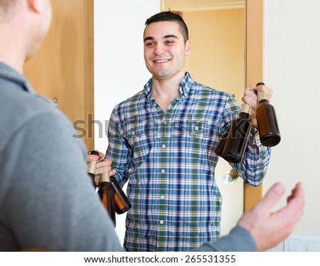 Guy meeting smiling buddy 35-40 years old with beer bottles at doorway