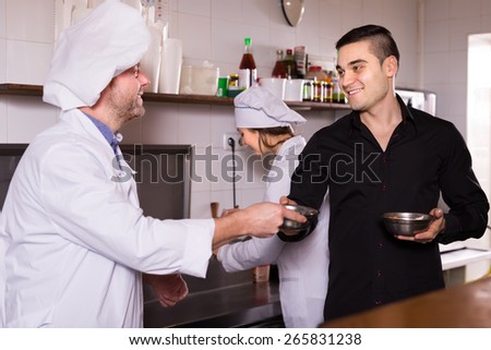 Portrait of happy young male waiter holding dishes and cooks at fastfood place