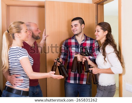Family couple welcoming happy adult visitors with beer bottles at home