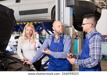 Young long-haired blonde girl duping by troubleshooters at auto service center. Selective focus