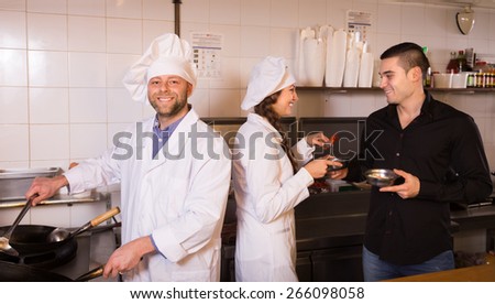 Smiling male waiter taking away prepared food at bistro kitchen. Focus on chef