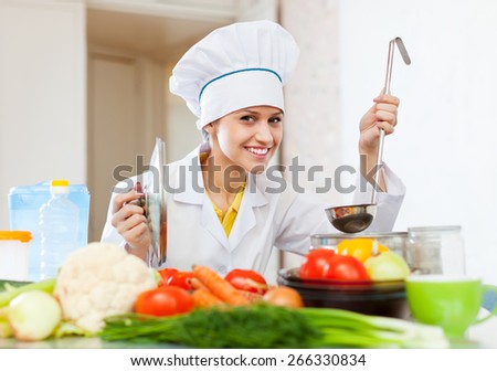 Happy  cook in white uniform tests soup from ladle at  kitchen