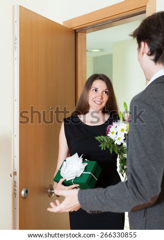 Girl giving flowers and gift to man at home door