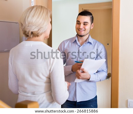 Mature woman answer questions of smiling guy with papers at door in home