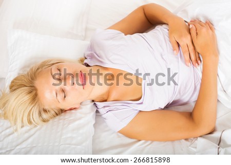 Middle-aged woman in pajamas sleeping with white pillow in bed at home