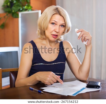Serios elderly woman filling in financial documents at table in home interior
