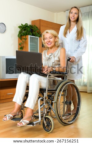 Happy woman in wheelchair with  assistant working on laptop indoor